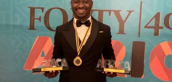 A person in a tuxedo holds two awards in front of a banner that reads FORTY | 40